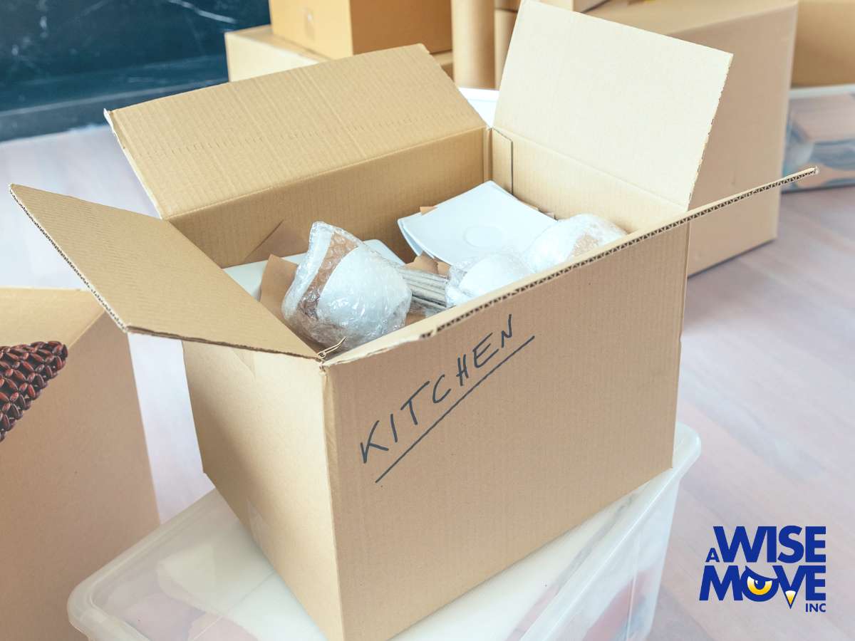 Box labeled 'Kitchen' showing carefully packed kitchen items with protective wrapping by A Wise Move.